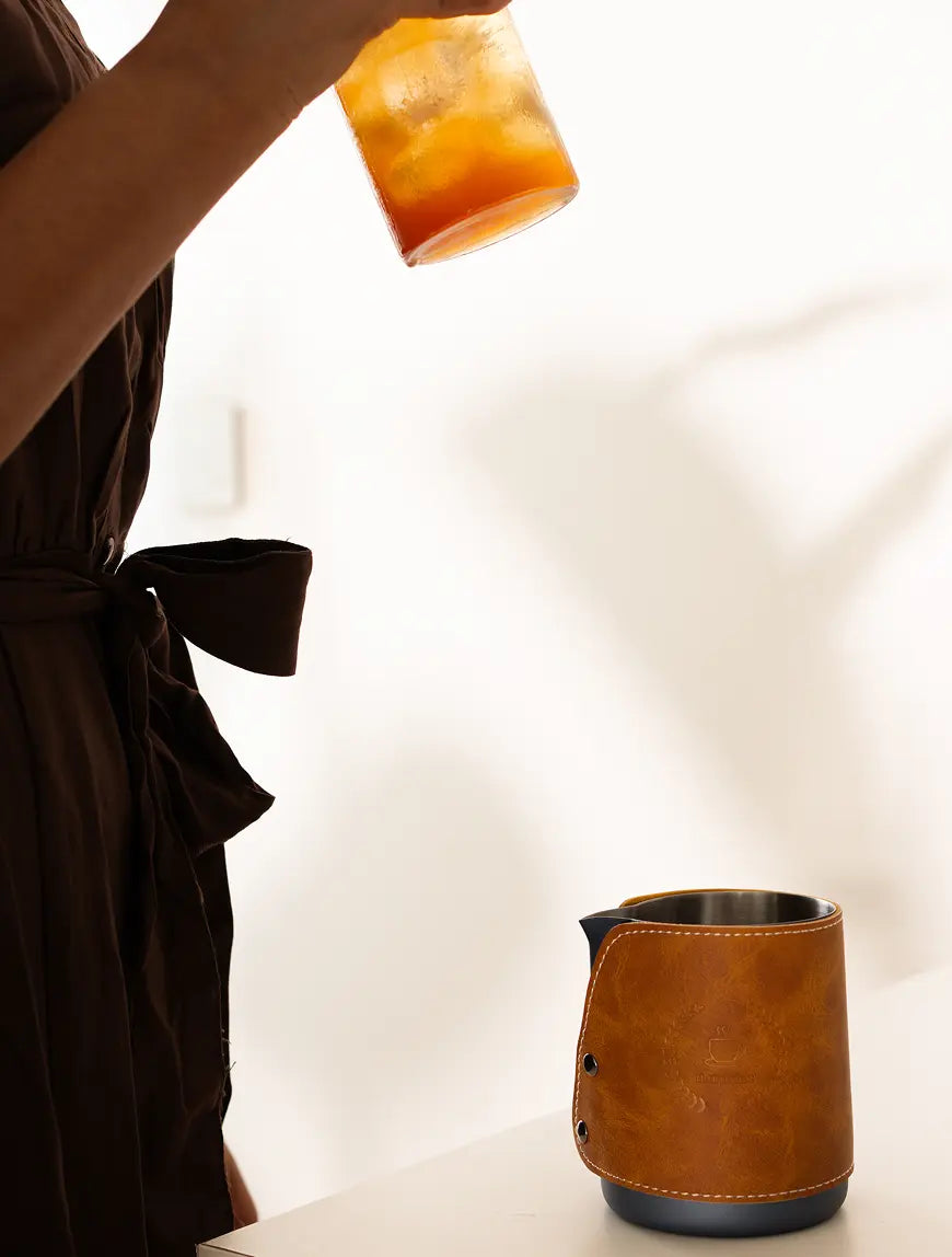 Brista Milk Pitcher with a brown leather wrap, stainless steel body, and a precise spout for controlled pouring.