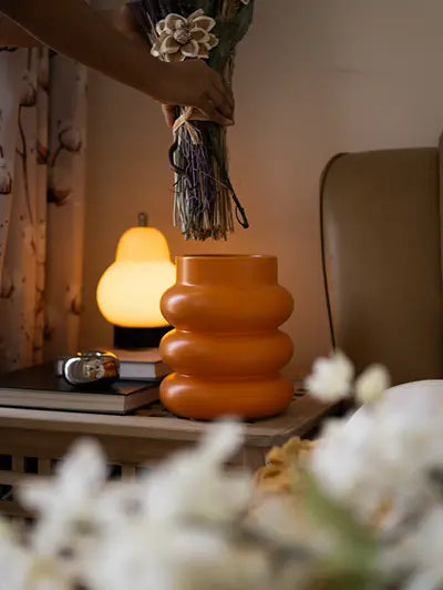 Hand placing dried flowers in orange ceramic vase – modern home decor on bedside table