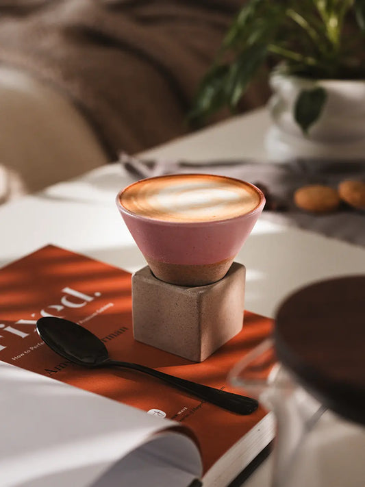 A pink Kono Ceramic Coffee Cup with a creamy latte, placed on an open book.