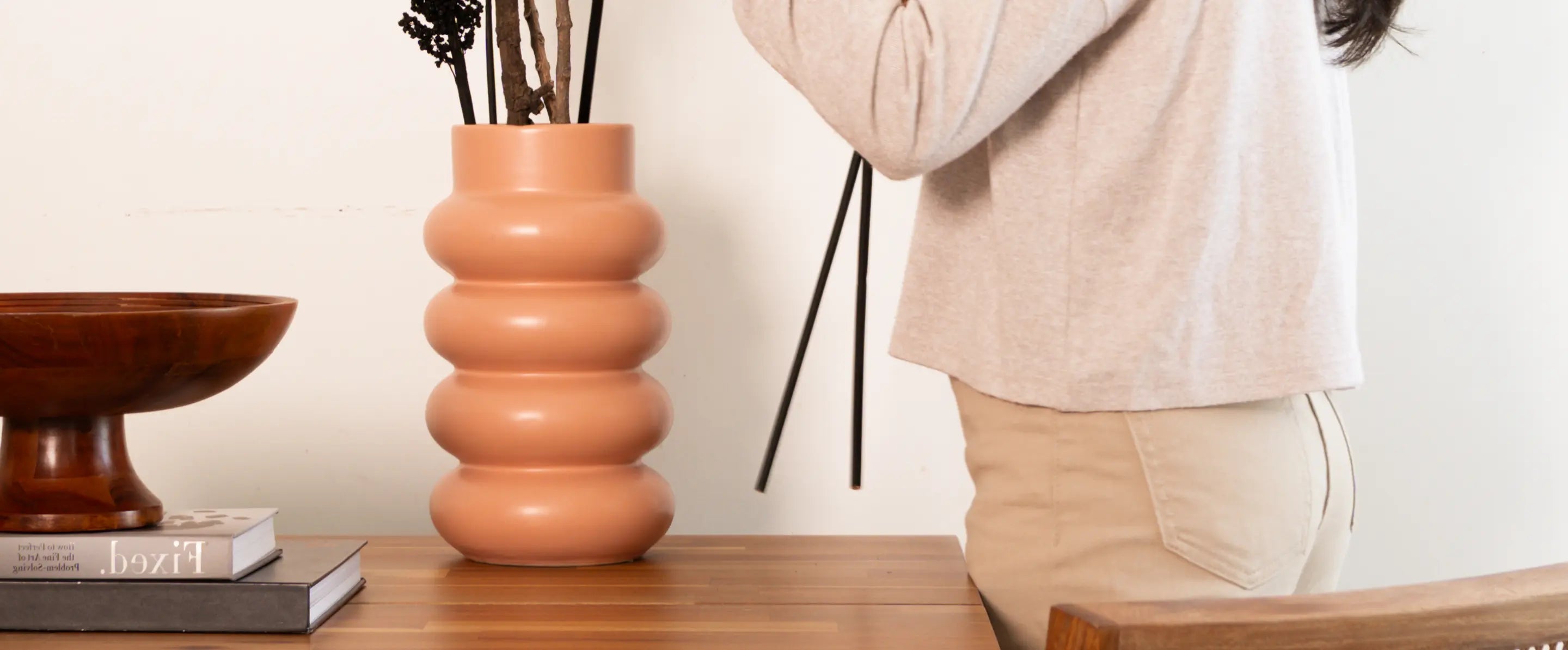 Orbit Ceramic Vase in peach with a sculptural silhouette, placed on a wooden surface beside a decorative bowl.