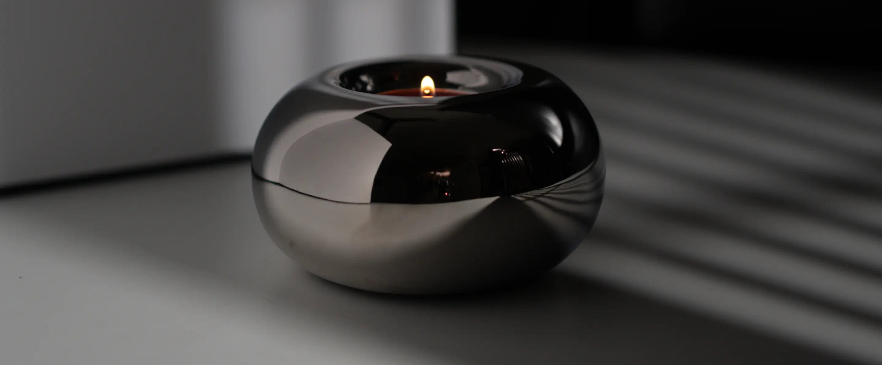 Donut Chrome Candle Holder with a lit tealight, placed in a moody, softly lit setting.