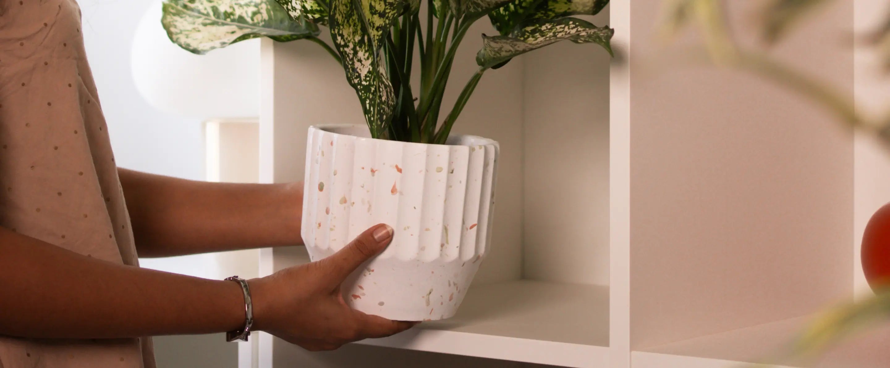 Hands placing the Marvellous Concrete Planter - White on a shelf, showcasing its terrazzo texture and elegant design.