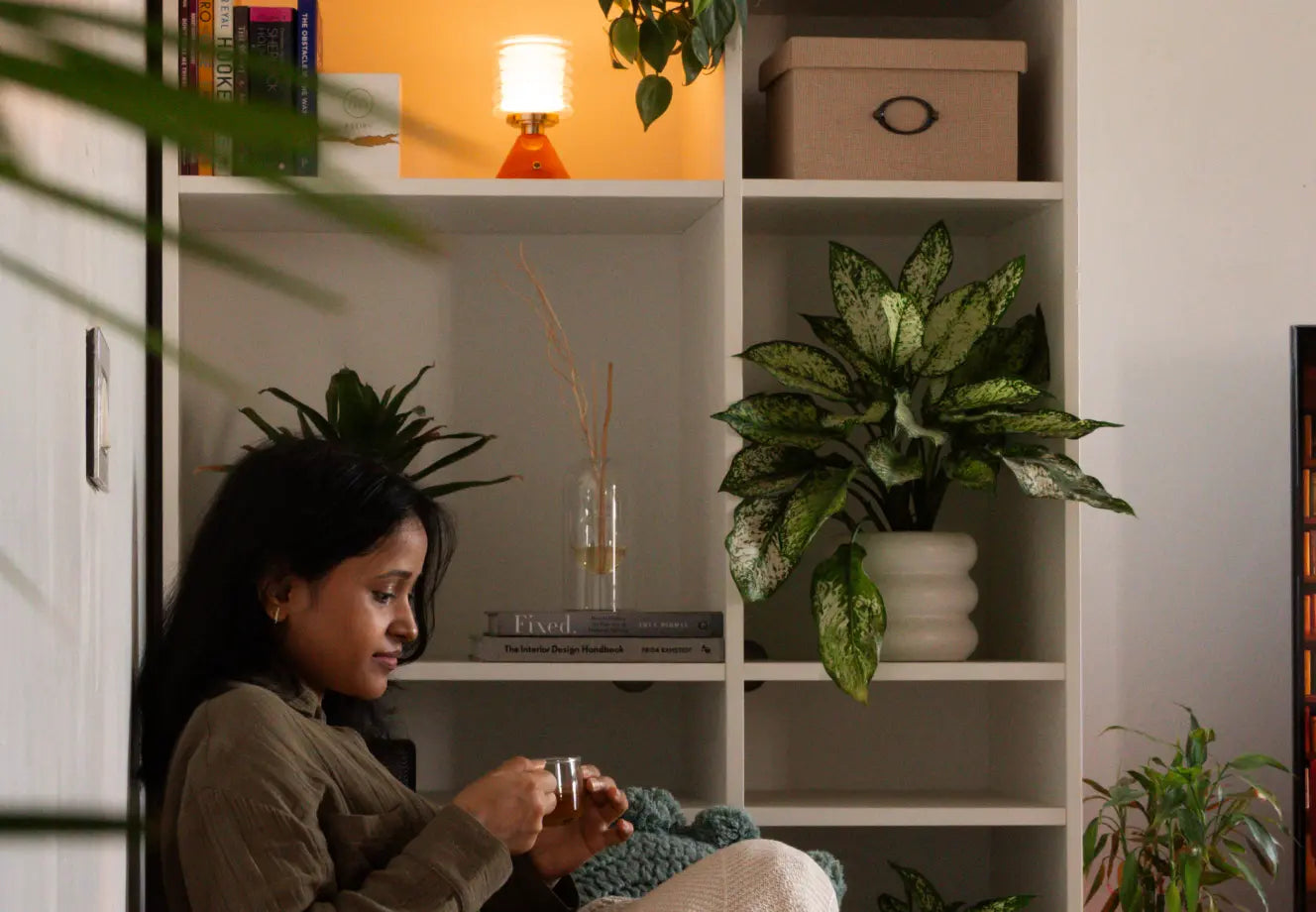 Woman enjoying tea in a cozy reading corner with warm lighting, indoor plants, and modern cozy home decor