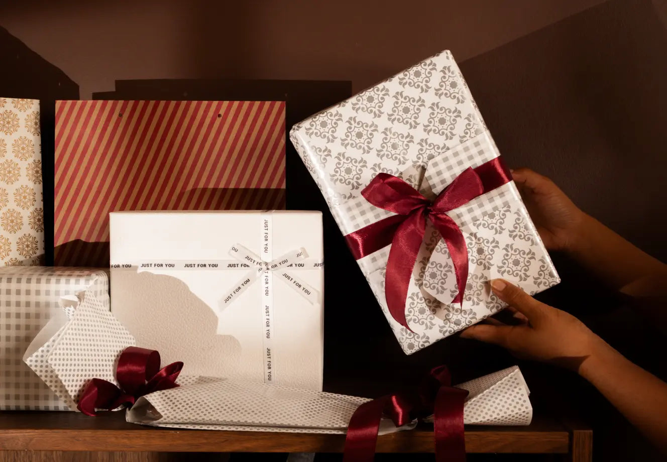 Beautifully wrapped Christmas gifts with red ribbons arranged on a wooden shelf, creating a warm festive gifting scene.