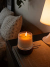 Lit scented candle on a design book beside a lamp – cozy home decor and home fragrance setup