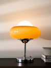 Modern orange glass table lamp with metal base glowing warmly on a dark wooden table