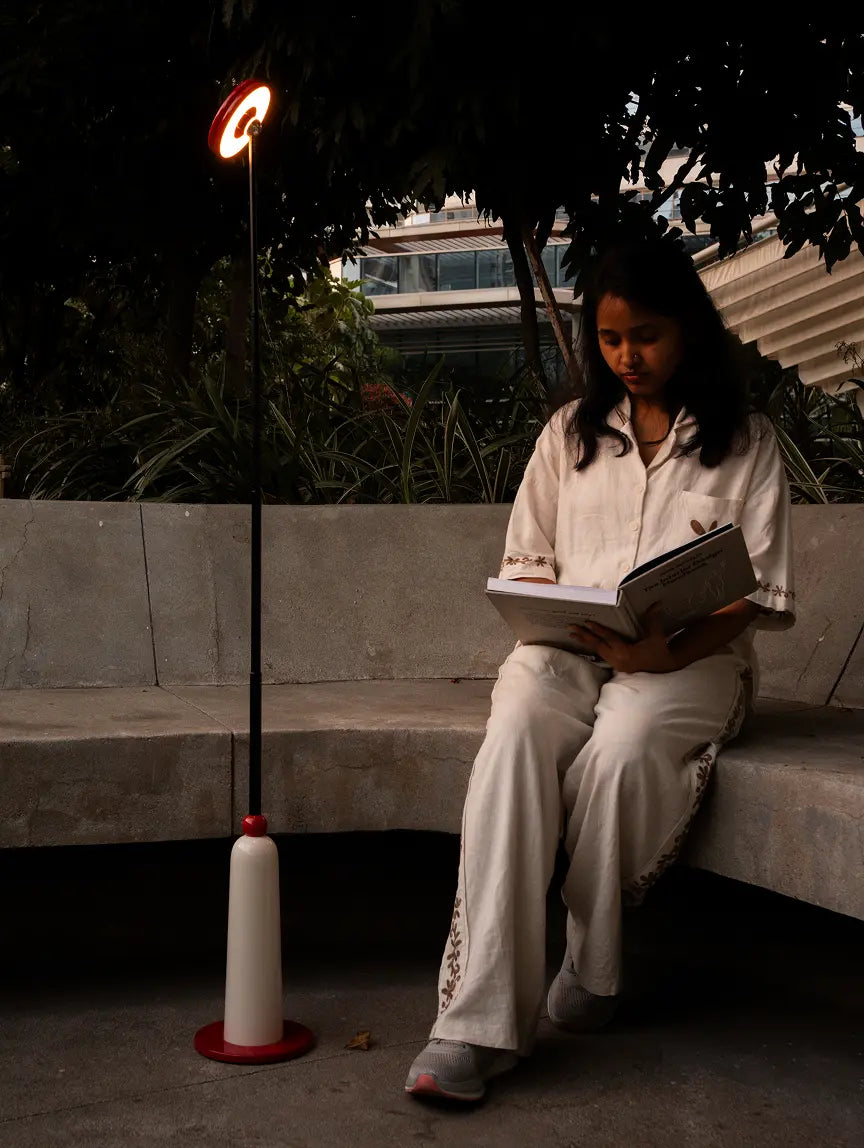 Girl reading outdoors beside Gharko 3-in-1 Frisbee Retractable cordless floor lamp with warm LED light.