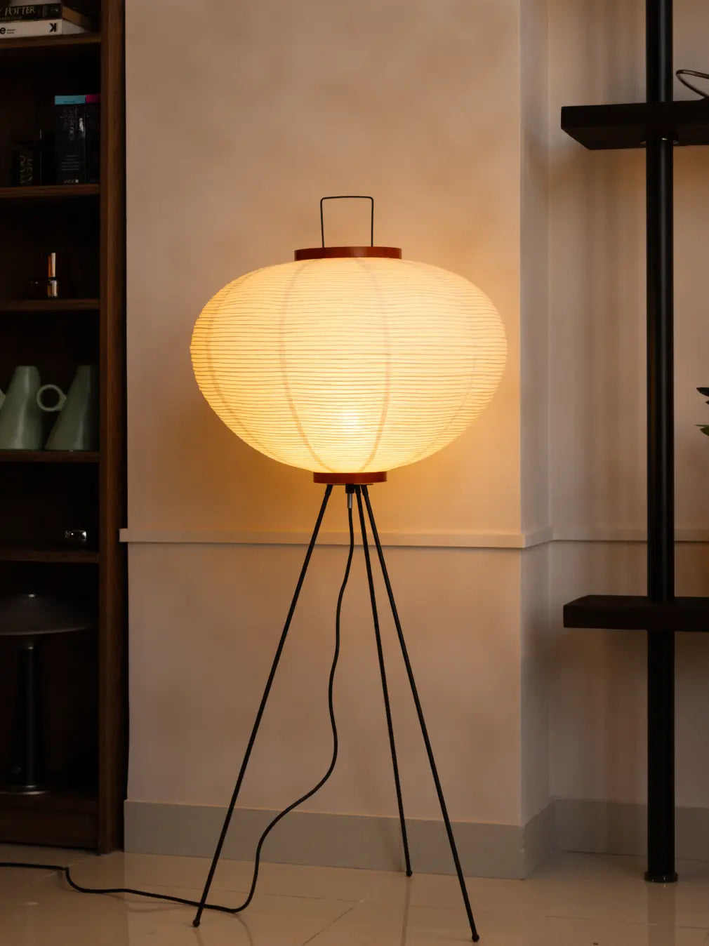 Akari Japanese Rice Paper Floor Lamp glowing warmly on a black tripod base in a modern living room.