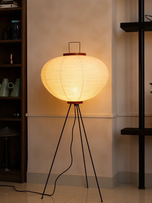Akari Japanese Rice Paper Floor Lamp glowing warmly on a black tripod base in a modern living room.