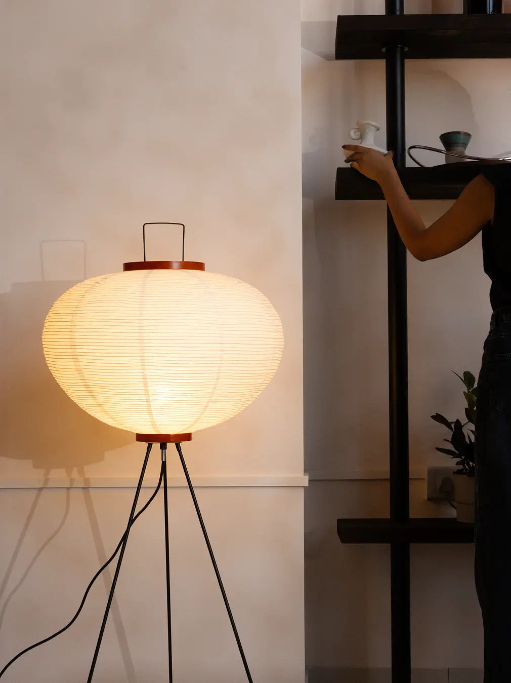 Akari Japanese Rice Paper Floor Lamp glowing softly as a person arranges decor in a modern home.