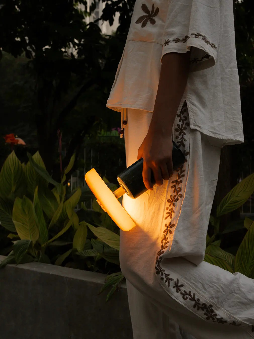 Person carrying the cordless Alba Moss Marble Table Lamp outdoors with warm amber glow