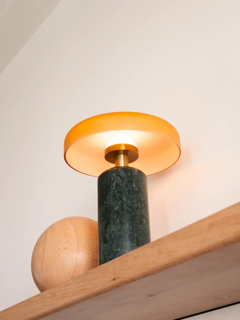 Close-up of the Alba Moss Marble Table Lamp glowing with its matte amber glass shade