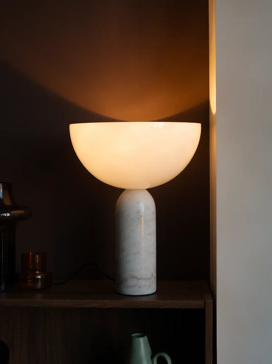 Arc Marble Table Lamp with a marble base and semi-circular glass shade on a dark shelf.