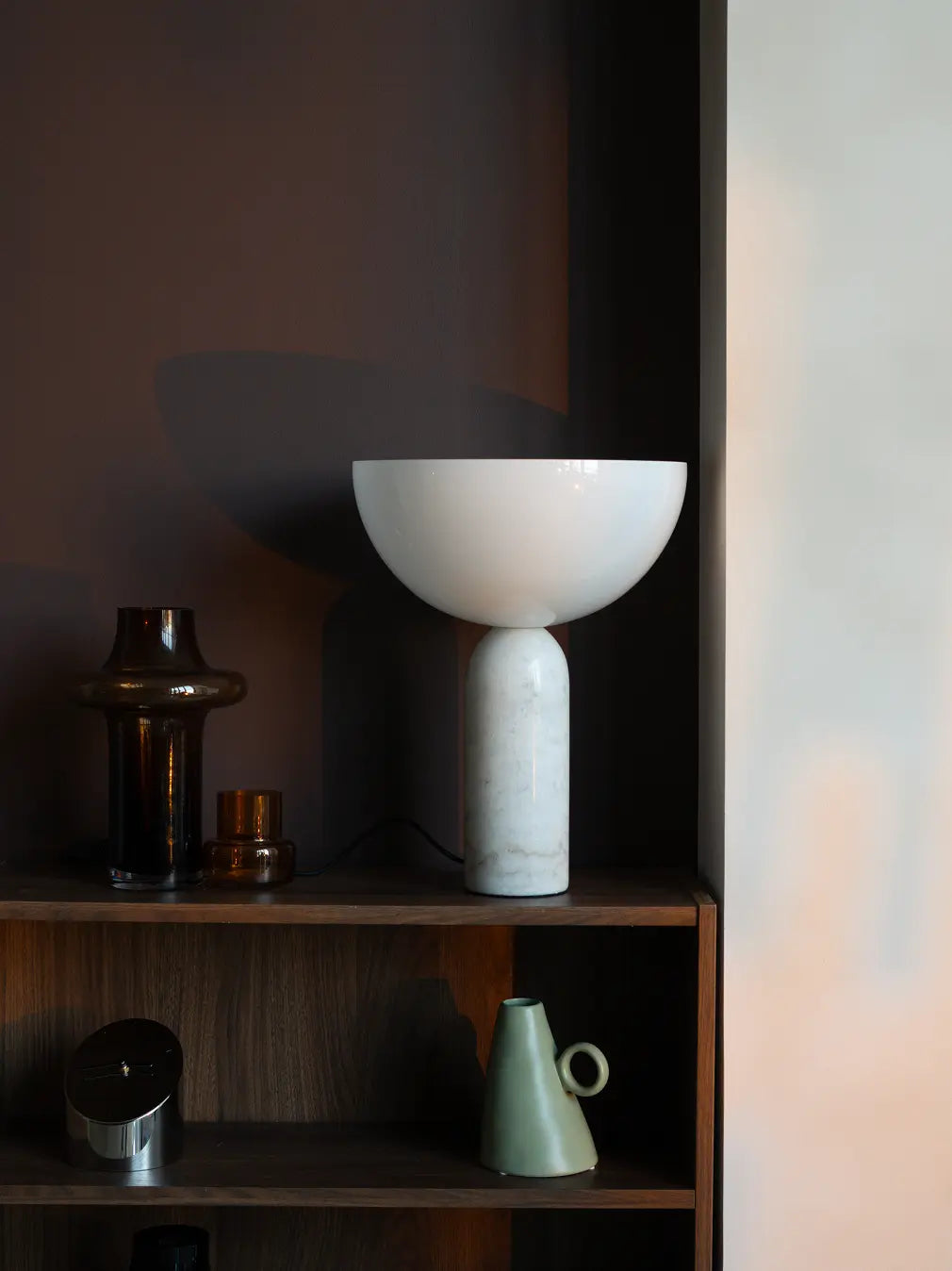 Designer table lamp with marble base and glass lampshade on a wooden shelf with a dark background
