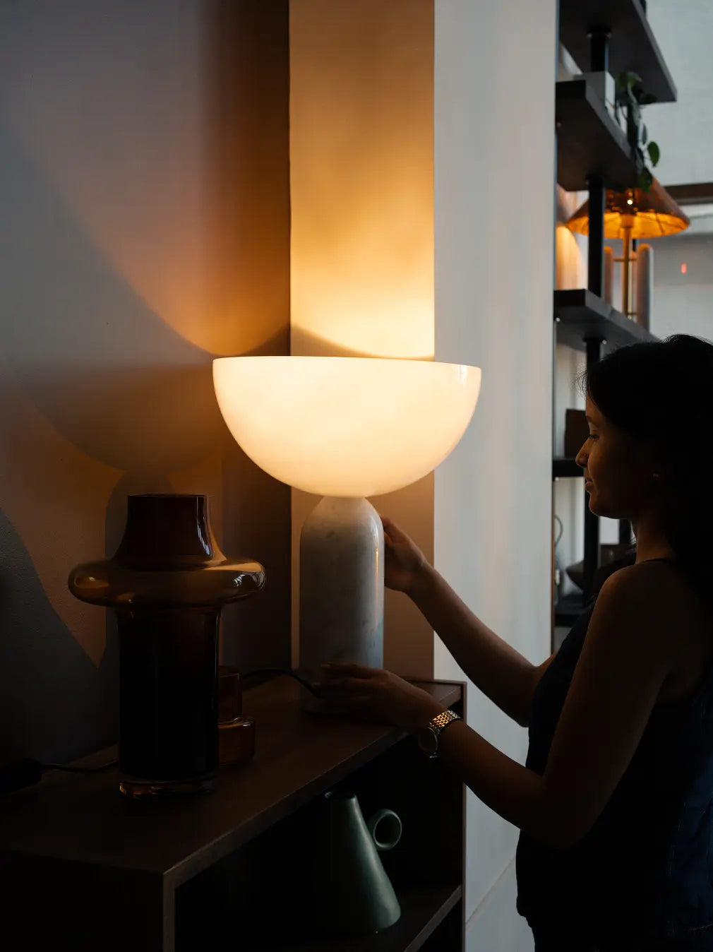 Woman styling Arc Marble Table Lamp on shelf, showcasing ambient light and sculptural form