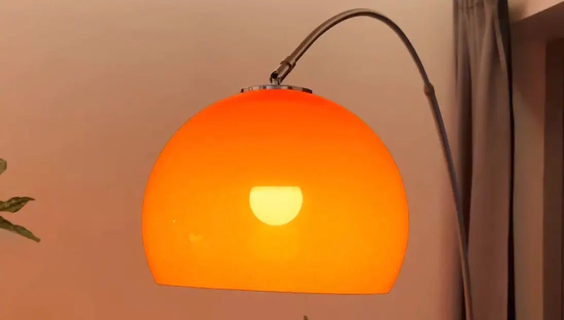 An arc floor lamp with a glowing orange dome shade and a curved metal arm, shown in a warm indoor setting.