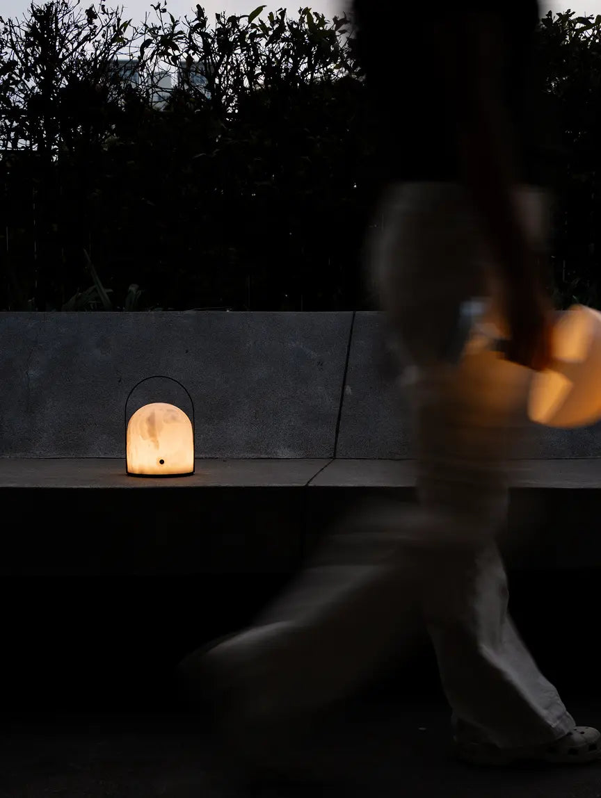 Arcus marble portable table lamp casting a warm glow beside outdoor seating