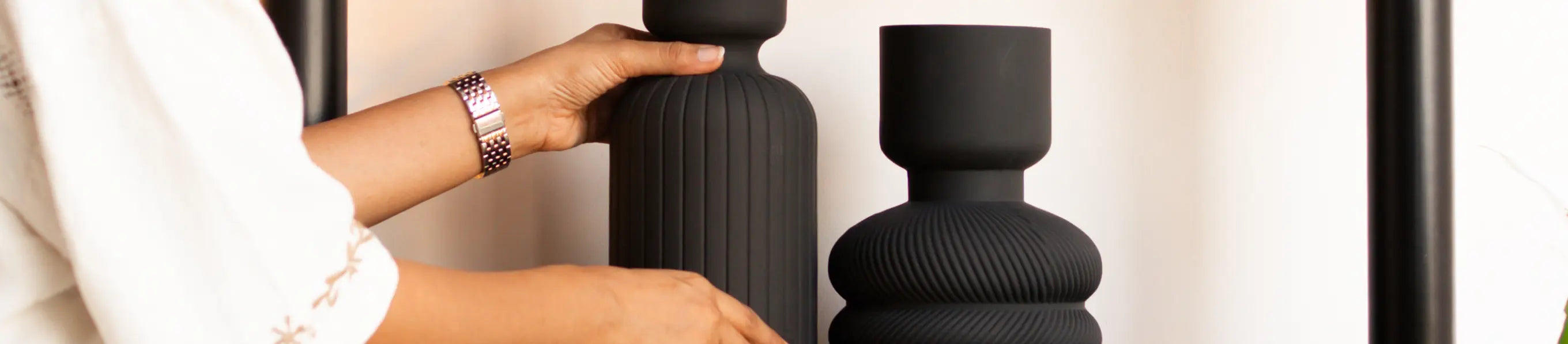 Person holding a black vase next to another black flower vase on a light background
