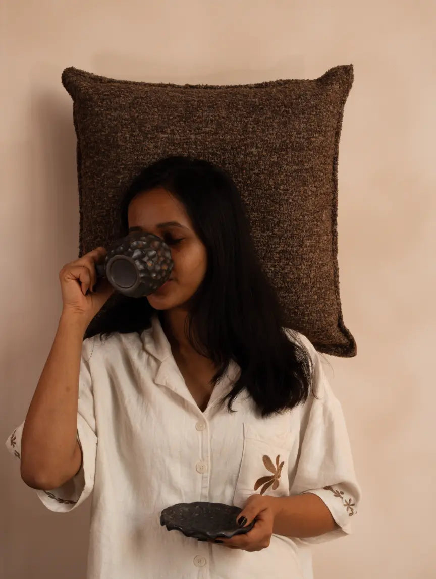 Woman drinking from a textured mug with a Gharko Boucle pillowcase behind her head against a beige background