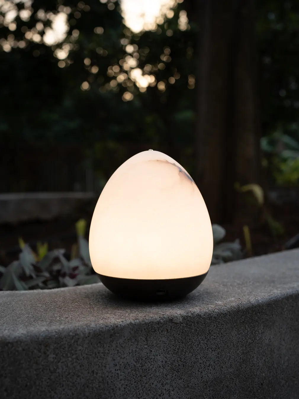 Bud Marble Portable Table Lamp casting a warm glow on an outdoor stone ledge