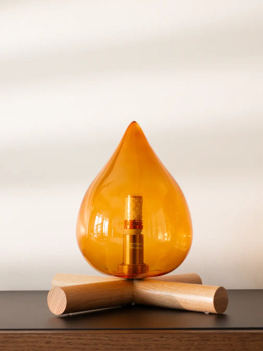 Campfire lamp with an orange teardrop-shaped with wooden base on a neutral background