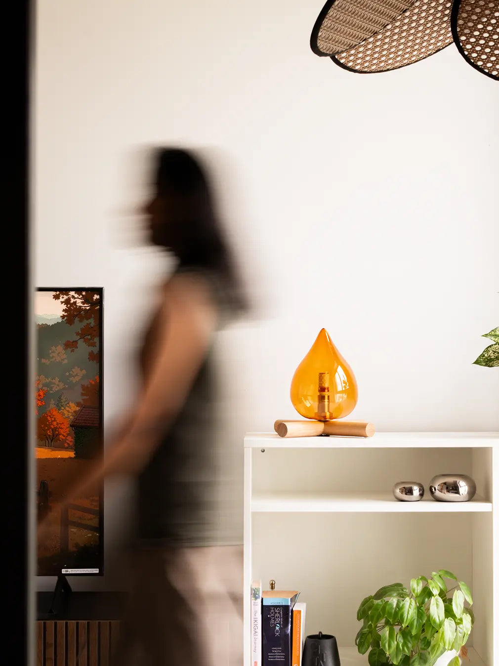 Person walking past a shelf with modern table lamp in a room.
