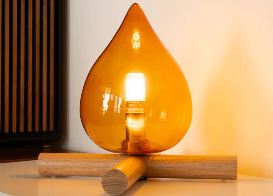 Decorative lamp with teardrop-shaped amber glass shade on a wooden base.