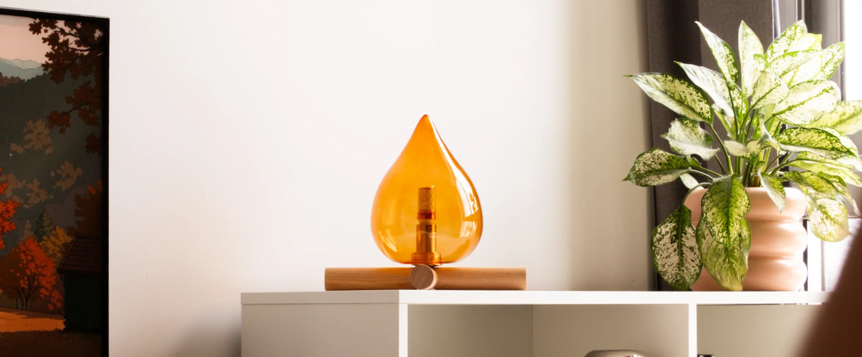 Decorative orange lamp on a shelf with a plant and a painting in the background