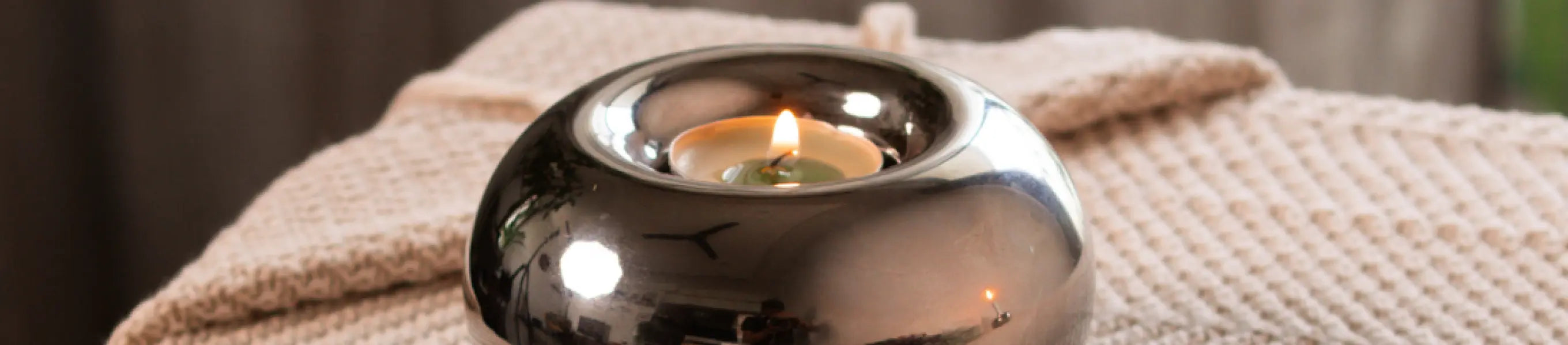 Round chrome candle holder with a tealight flame, styled on a textured beige throw in a cozy home setting.