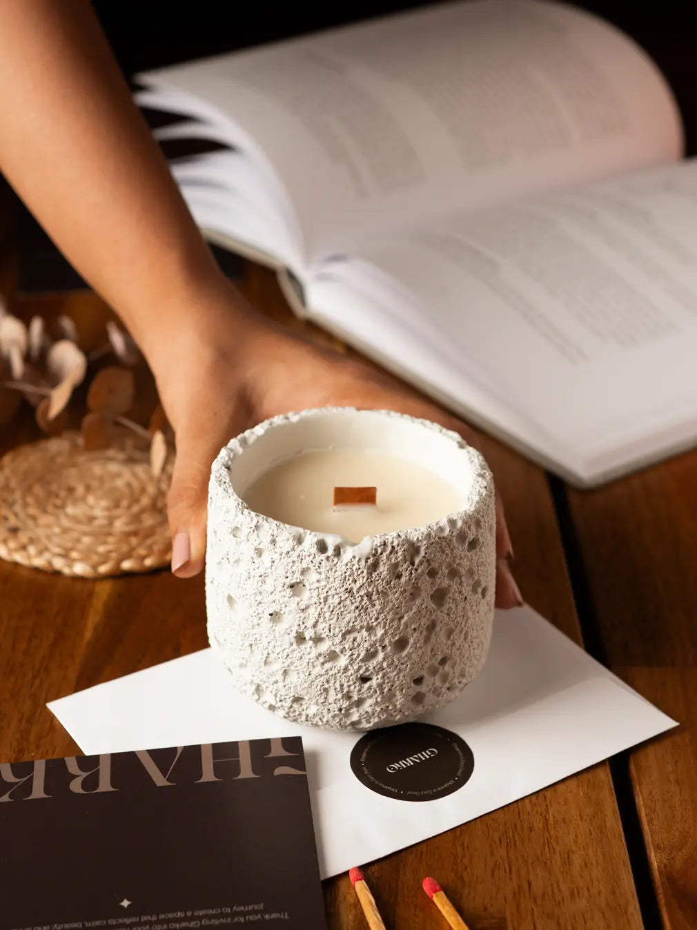 Capri concrete scented candle on a wooden surface with a book and matchsticks.