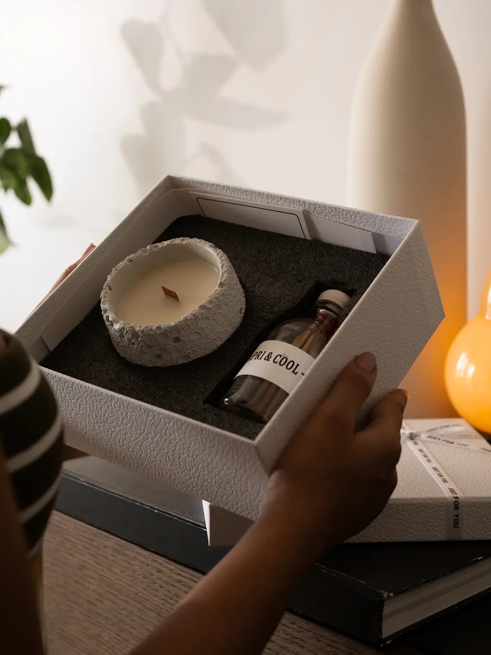 Candle and bottle set in a box held by a hand, with a blurred background
