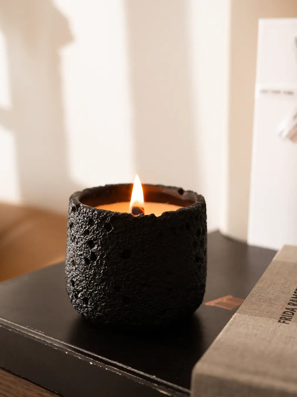 Black Capri Concrete Scented Candle lit on a side table, handmade with soy wax and wood wick
