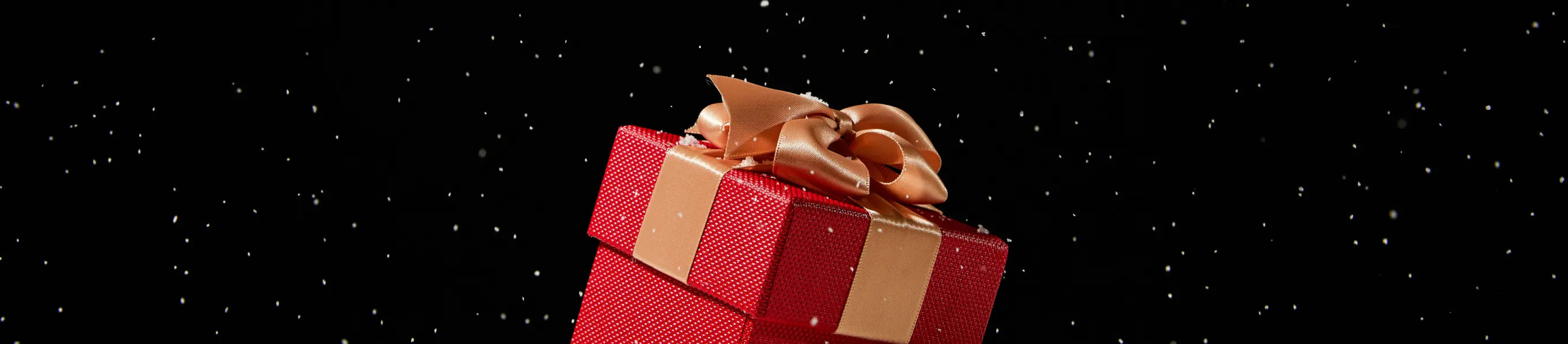 Red gift box with a gold bow on a black background, perfect for Christmas gift.