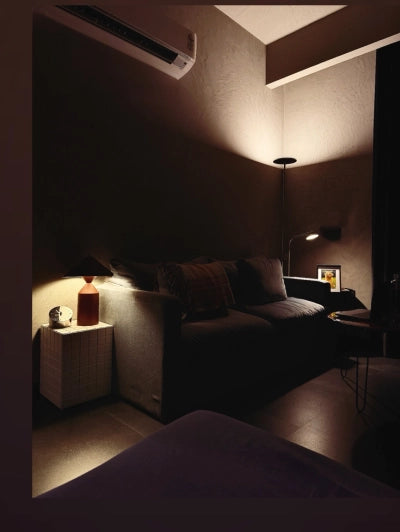 Dark living room with a sofa, lamp, air conditioner, and a table clock