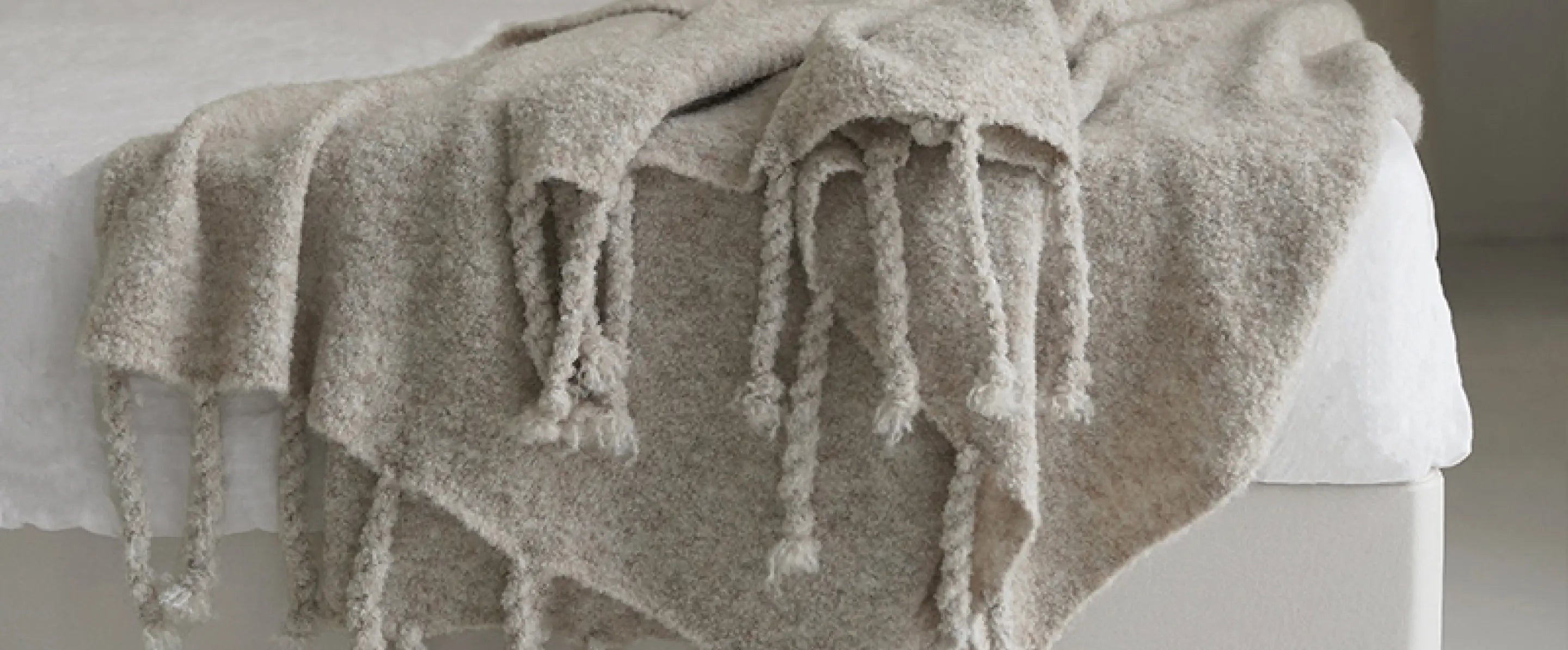 Apricot grey wool bed throw blanket draped on bed showcasing tassels and knit detail