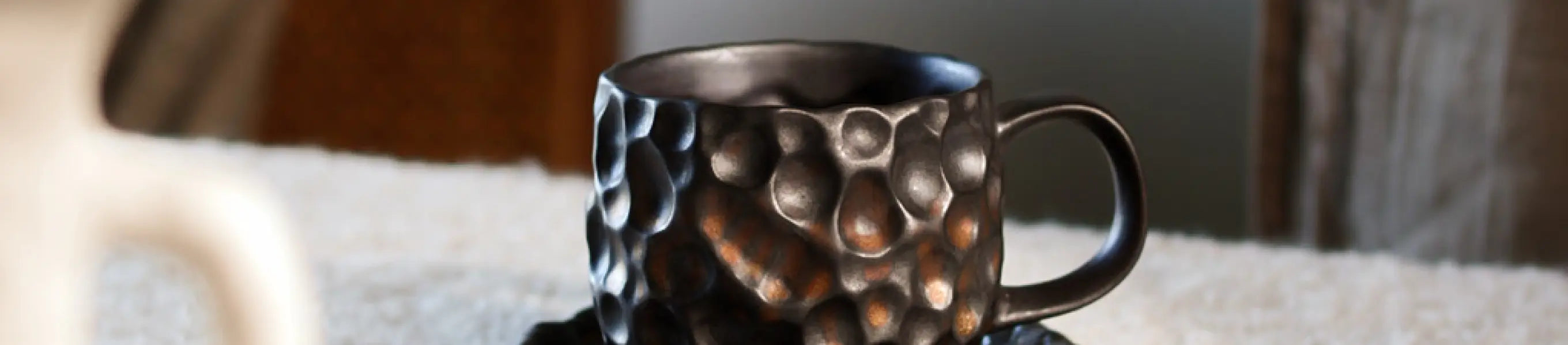 Black textured coffee mug on a light surface with a blurred background