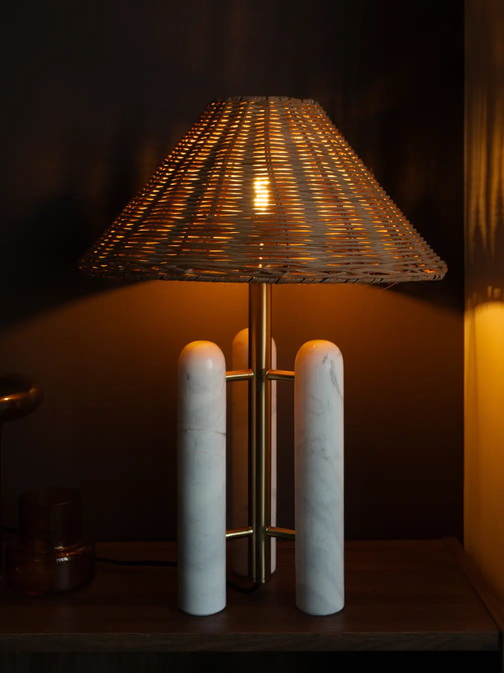 Decorative lamp with rattan shade and marble base on a dark background