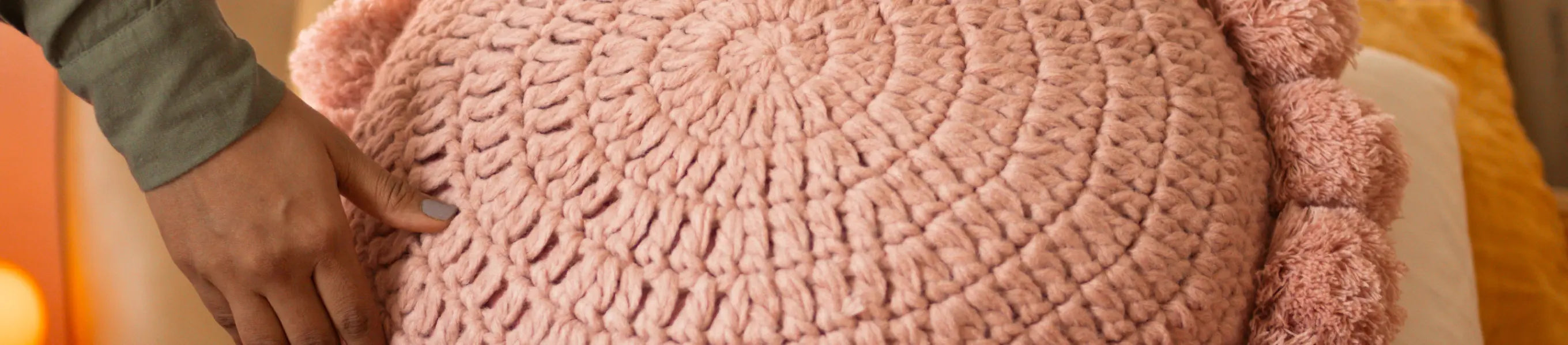 Pink textured cushion being held by a hand on a blurred background