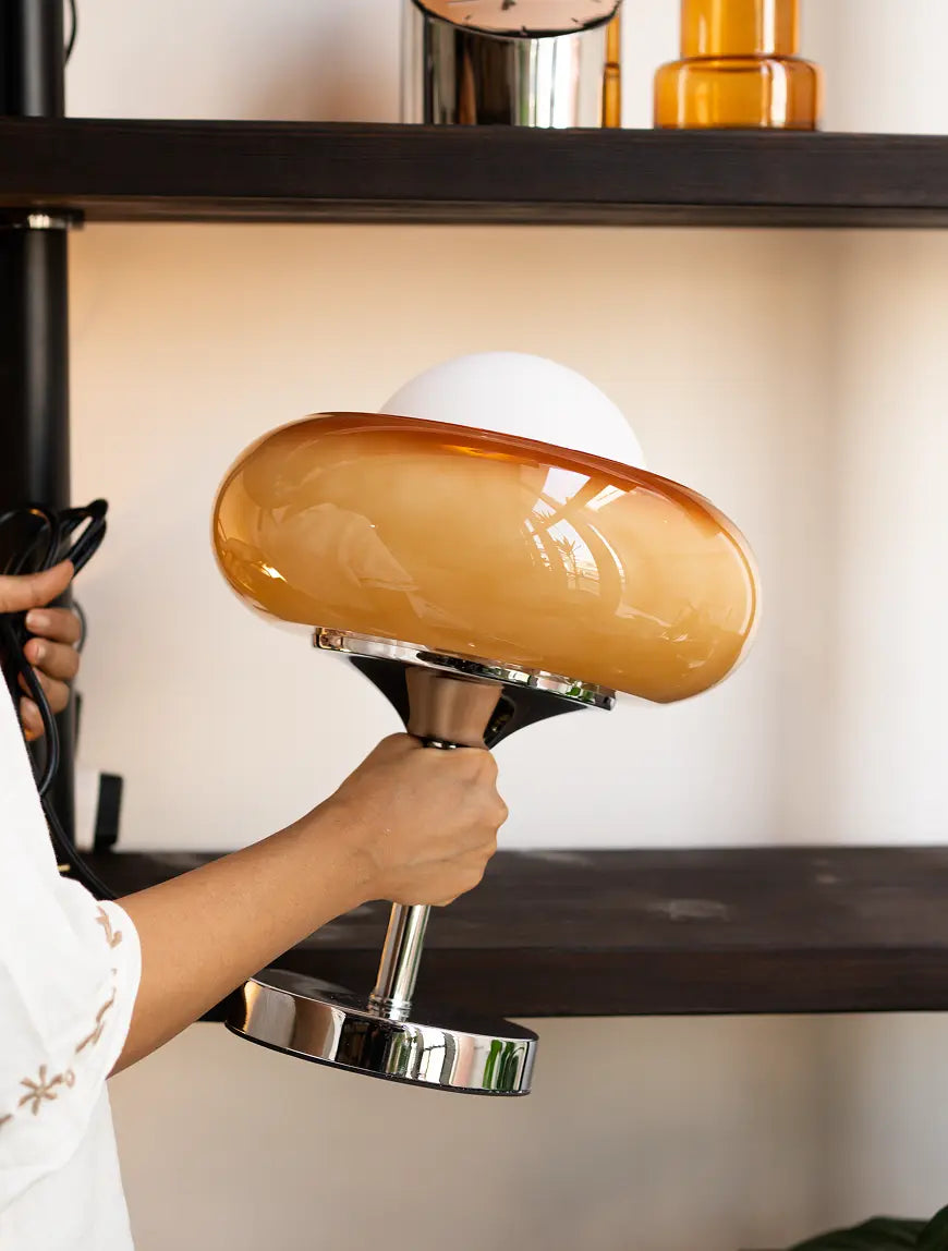 Placing the Dawn Glass Table Lamp on a living room shelf, highlighting its modern glass design and warm ambient glow.