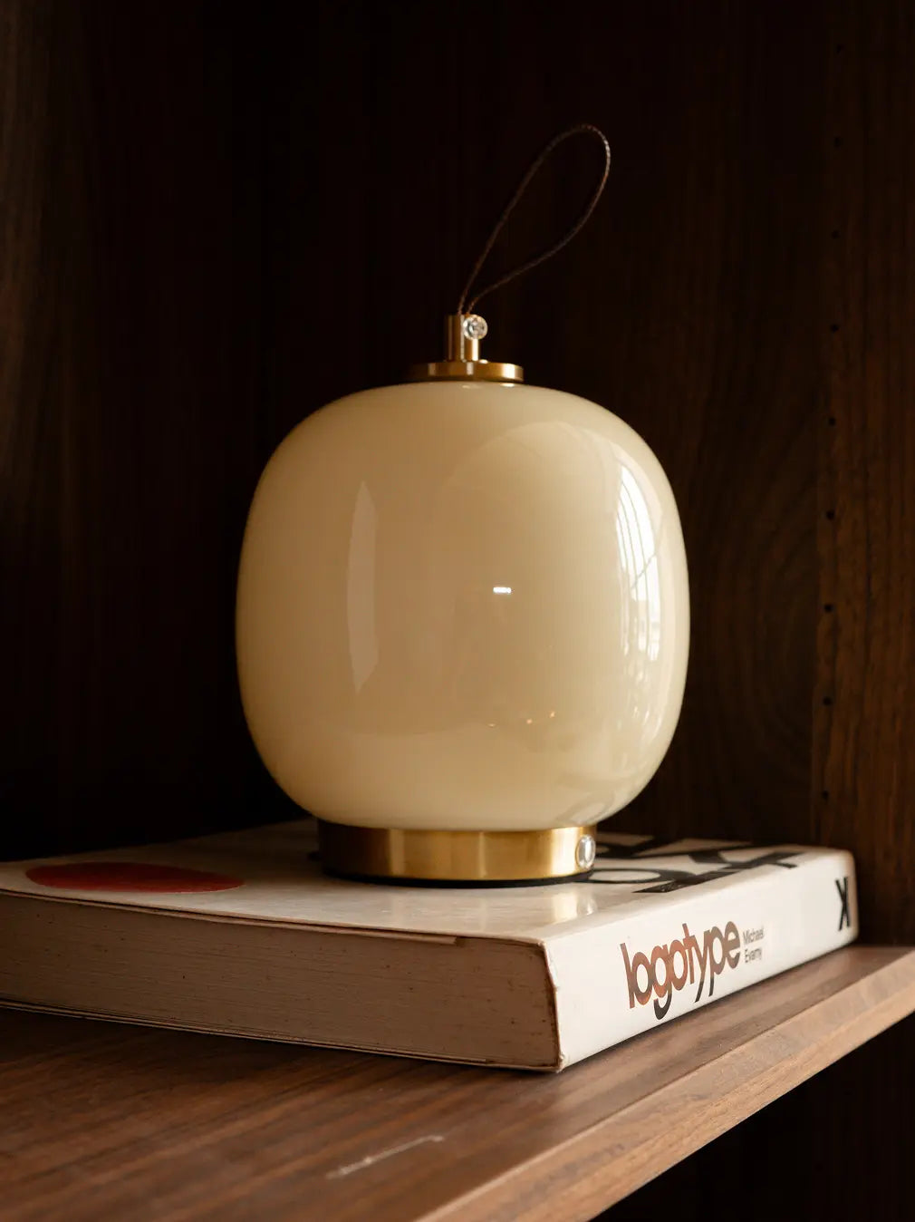 Light yellow Dew glass table lamp with leather strap styled on a wooden shelf