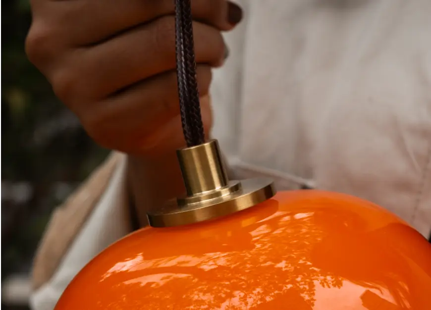 Close-up of orange Dew portable glass lamp with leather carry strap