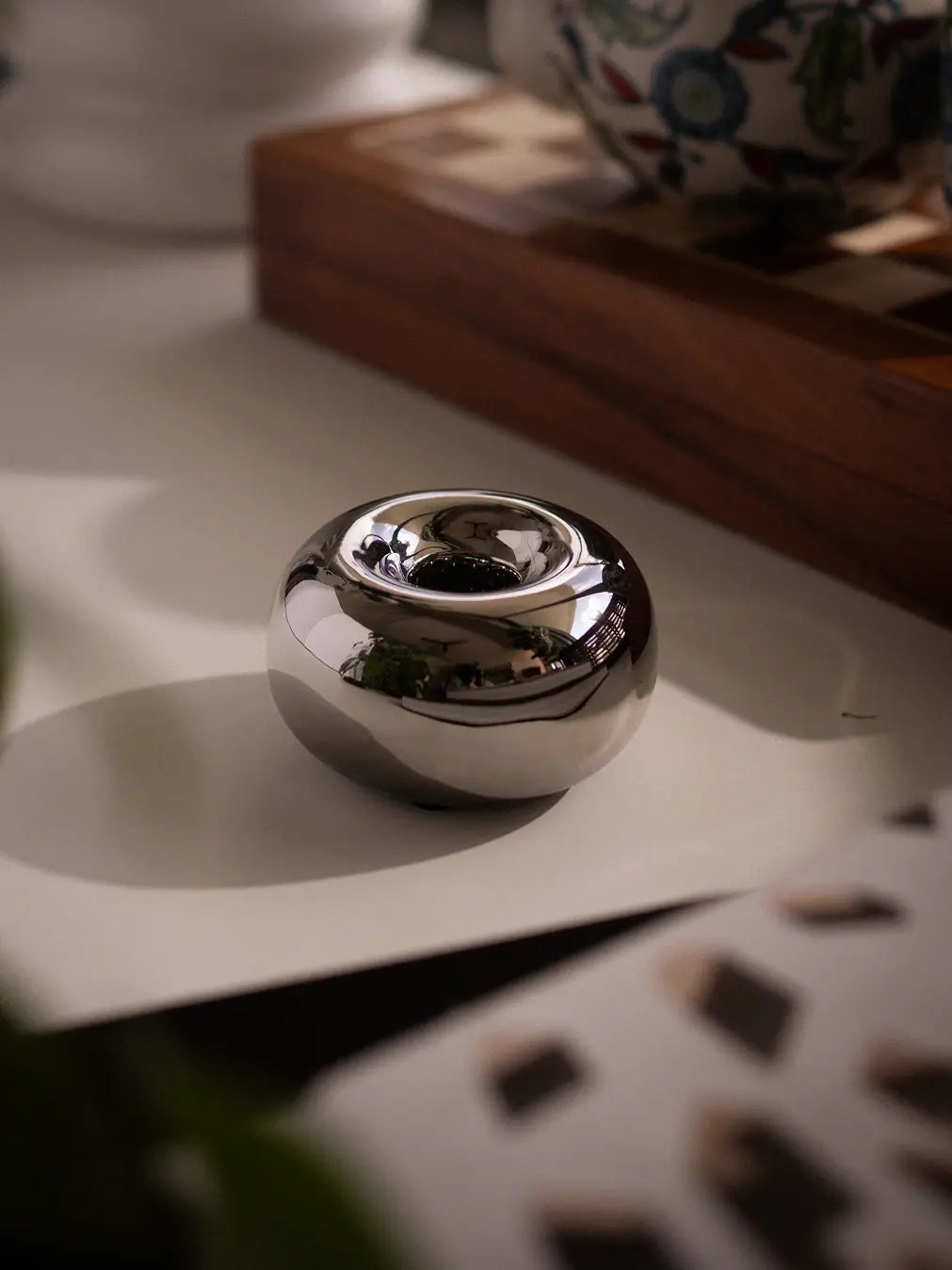 Donut Chrome Candle Holder with a polished silver finish, placed on a white surface with warm reflections.