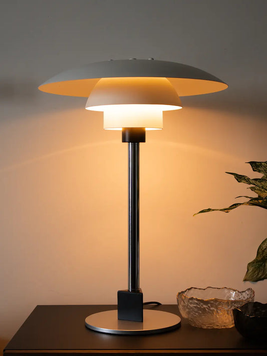 Echo Metal Table Lamp with white layered shade and silver base lit on dark tabletop