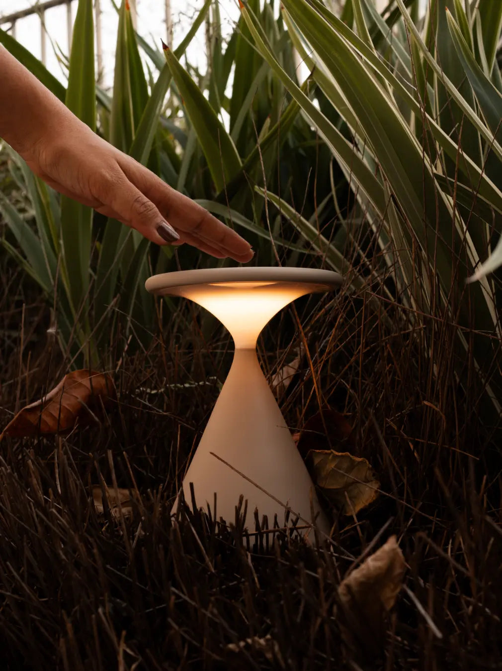 Hand using Flux Portable Table Lamp in outdoor garden setting with warm LED light