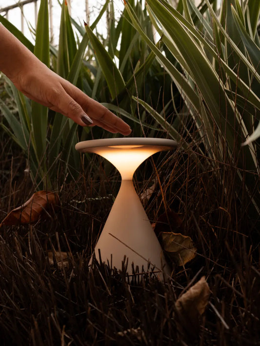 Hand using Flux Portable Table Lamp in outdoor garden setting with warm LED light