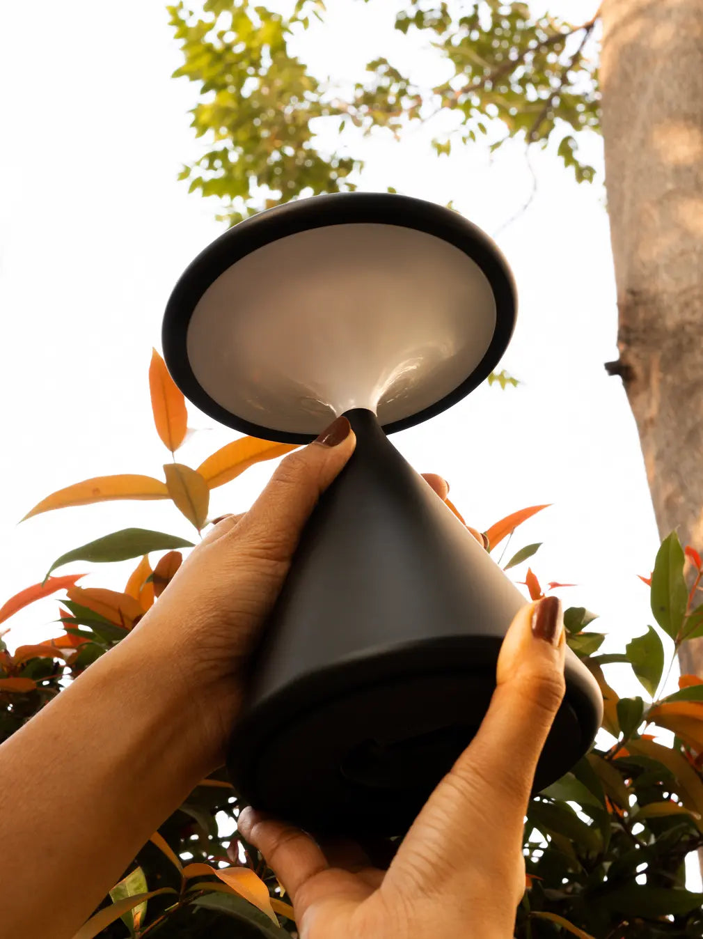 Close view of black Flux Portable Table Lamp held outdoors showing sculptural design