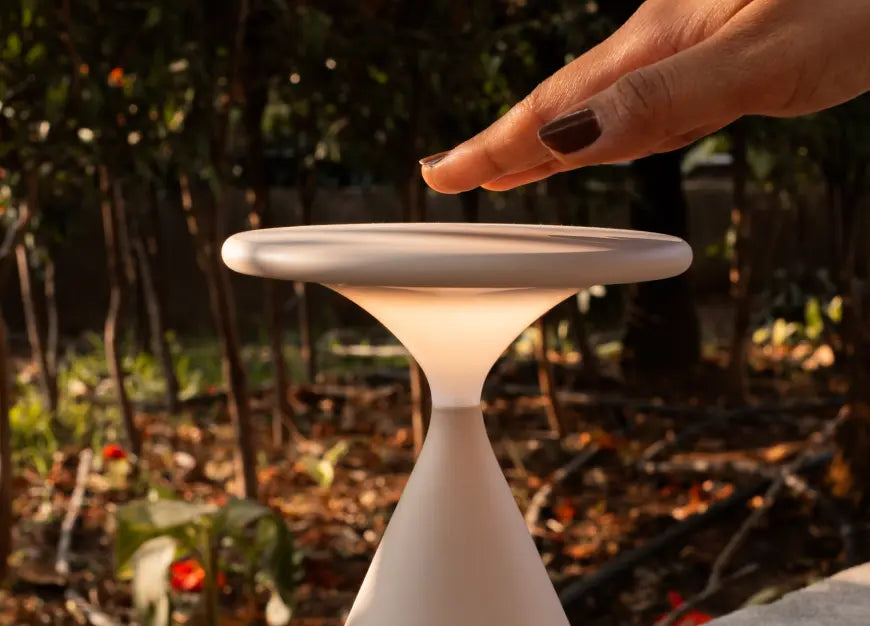 Close up of hand using top touch control on Flux Portable Table Lamp in bone color.