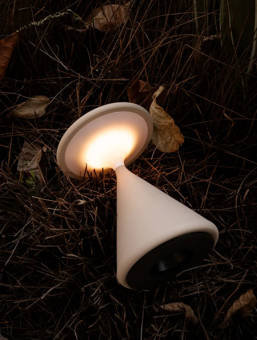 Bone colour Flux Portable Table Lamp glowing softly while placed on natural ground.