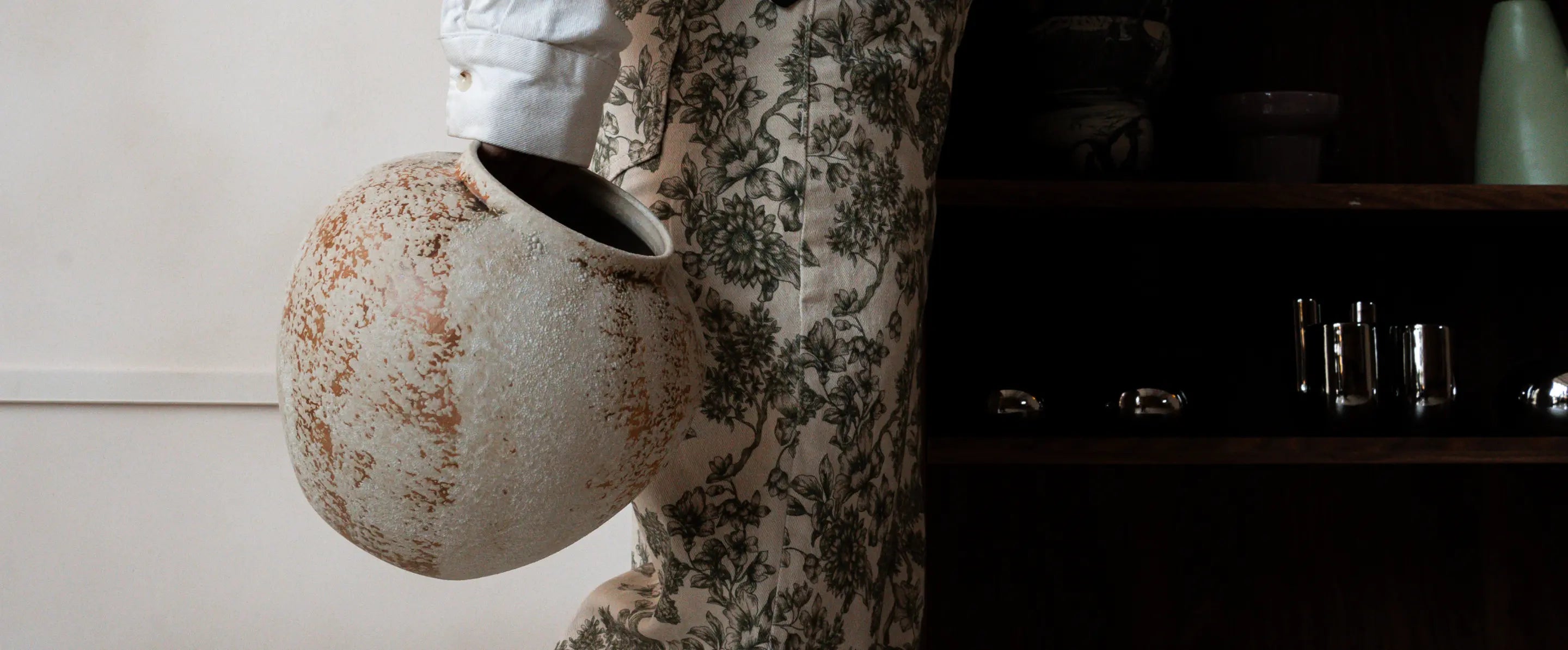 Person holding a ceramic flower vase with floral pattern in a room setting