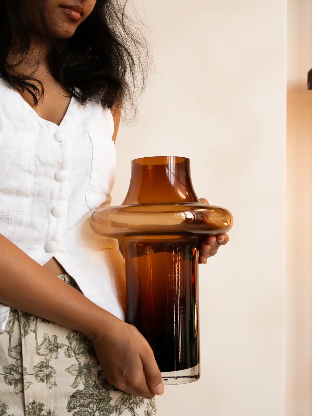Person holding a large amber glass vase against a neutral background